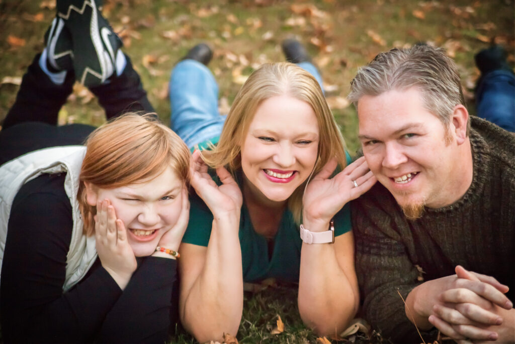 Playful fine art family portrait lying in the grass, capturing genuine laughter and connection.