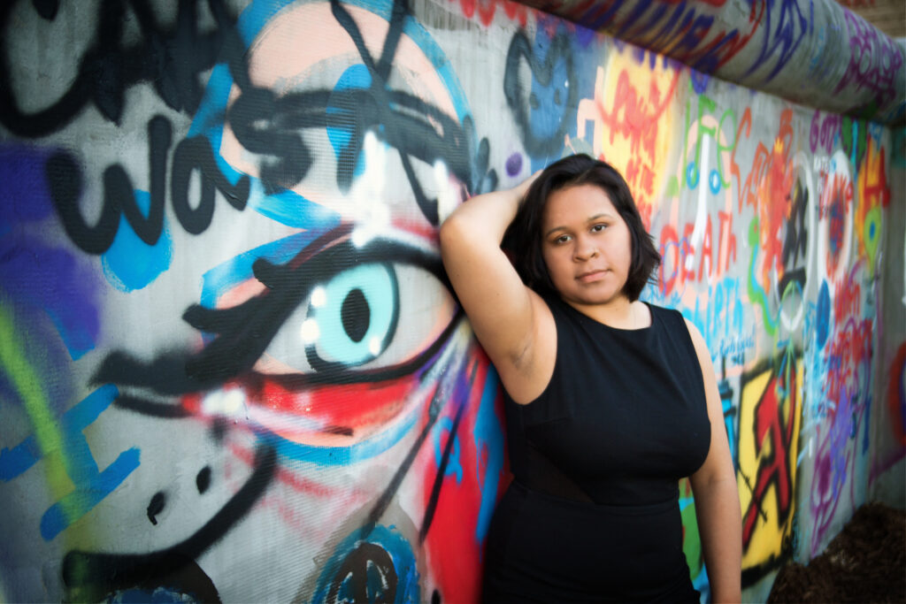 Bold fine art portrait of a woman in a black dress against a vibrant, colorful graffiti wall, urban portrait photography.